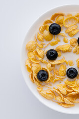 top view of corn flakes in bowl with organic milk and fresh blueberries isolated on white.