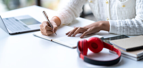 Cropped shot of Asian woman hand using laptop and writing making list taking notes in notepad...