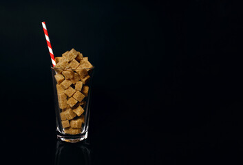 Cane sugar slices in a glass with a red and white drinking straw on a black background. The notion of how much sugar is in sodas, soft drinks, and sweets is dangerous. Free space for text and ads