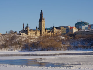 Gothic revival buildings and towers of parliament hill, seen from the park along Ottawa river on a sunny witer day with clear blue sky. Ontario, Canada 
