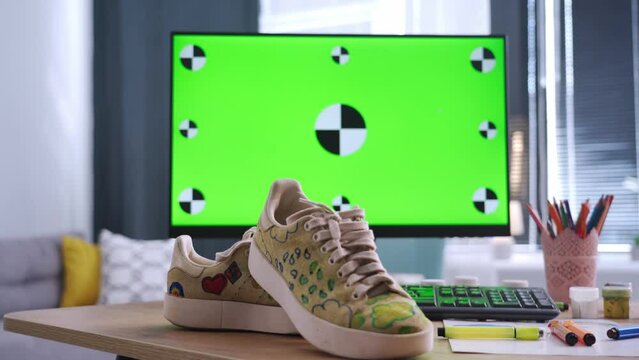 shoes design, a monitor with a green screen stands on a table with paints and sneakers stands in a modern room
