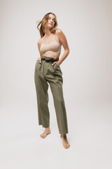 Fototapeta premium Beautiful woman with long curly hair and natural makeup wearing crop top and casual trousers posing over white background.