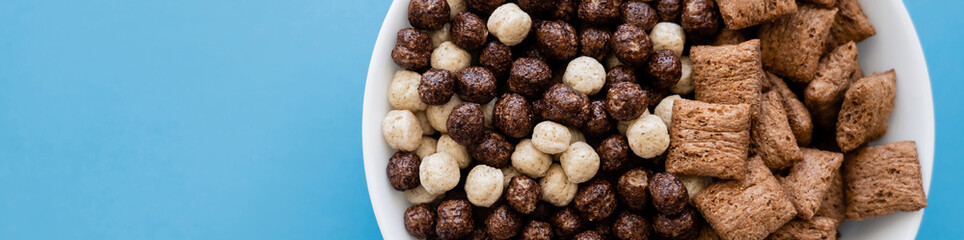 top view of bowl with tasty cereal balls and puffs isolated on blue, banner.