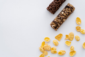 top view of crunchy corn flakes near tasty granola bars isolated on white.