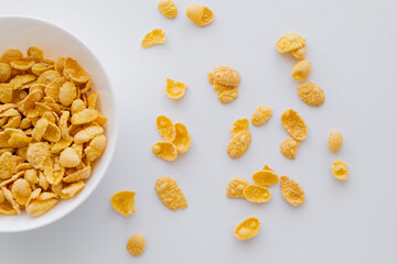 top view of crispy and yellow corn flakes near bowl isolated on white.
