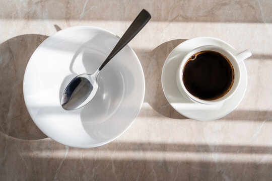 top view of cup of black coffee near white saucer with spoon on marble surface.