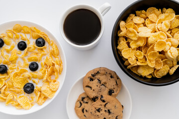 top view of bowls with corn flakes in milk with blueberries near cup of coffee and chocolate chip...