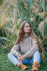 Beautiful young woman with long hair and brown eyes in the autumn park. Portrait of a model in a knitted sweater near the pampas grass. Fall.