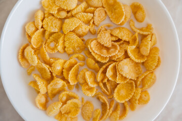 close up view of bowl with corn flakes and organic milk on marble surface.