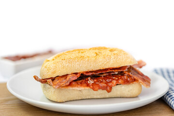 Closeup of crispy bacon in a sourdough roll on white plate