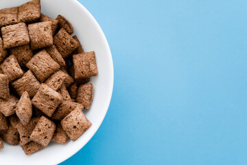 top view of chocolate cereal puffs in white bowl isolated on blue.