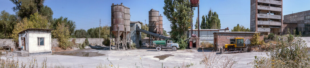 Fototapeta na wymiar Panoramic photo of an old cement factory. An old dump truck and tractor made in the USSR.