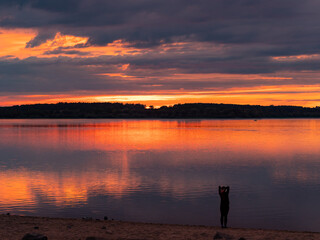 Silhouette of a stretching woman at the beach. Doing sport during a sunset at the beach. Beautiful orange sunlight is in the evening sky which is reflected in the calm lake.