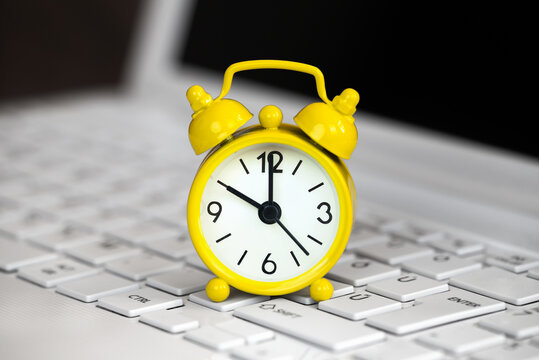 Yellow alarm clock on a white laptop, daylight savings time background