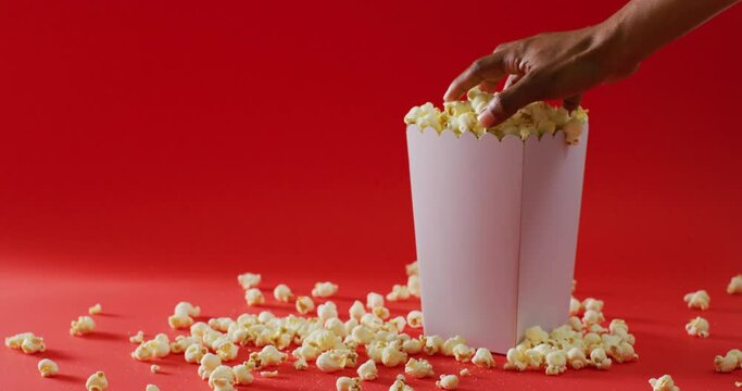Video of close up of hand and popcorn on red background
