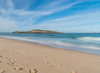 View of empty Praia da Ilha do Pessegueiro sand beach with with long exposure blurred ocean waves and Fort of Pessegueiro small island at Rota Vicentina coast near Porto Covo, Portugal.
