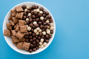 top view of bowl with tasty cereal balls and puffs isolated on blue.