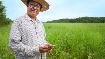 A farmer is using a mobile phone standing in a field against a green field backdrop.