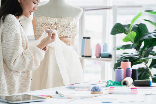Selective focus on hand of attractive 30s woman fashion designer or dressmaker touching textile fabric texture after fitting new evening dress collection on a mannequin, working at workplace studio