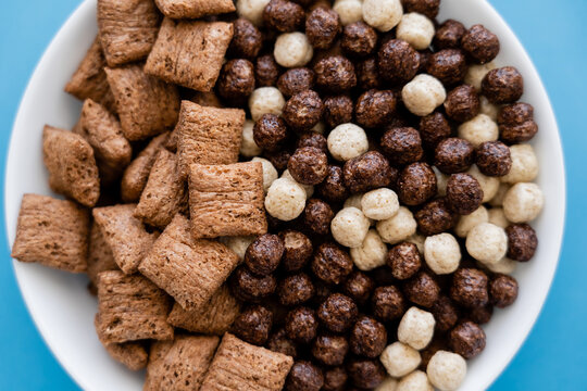 close up view of bowl with tasty cereal balls and puffs isolated on blue.