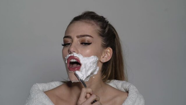 Woman shaving face. Beautiful young caucasian woman shaving her face by razor. Pretty girl with shaving foam on her face.