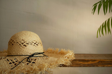 Mockup of a straw tropical hat on a wooden cantilever shelf against a wall with a palm tree branch and tree shadow.