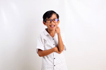 Happy asian boy standing while pointing and looking at the camera. Isolated on white background