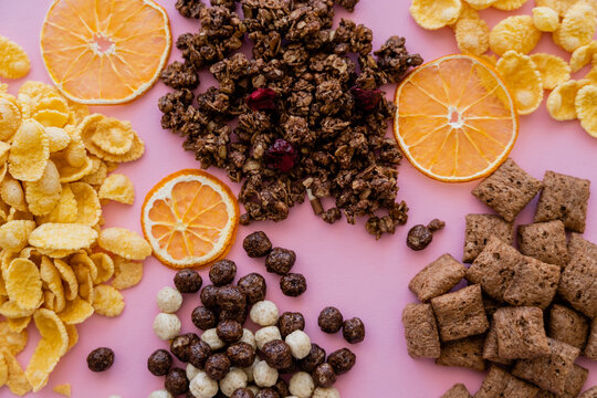 top view of various breakfast cereal corn flakes, puffs, balls and granola near dried oranges on pink. © LIGHTFIELD STUDIOS
