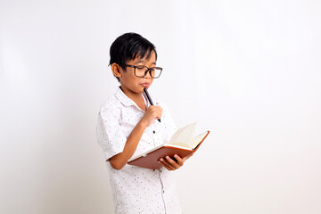 Naklejka premium Smart asian schoolboy thinking while holding a book and a pen. Isolated on white background