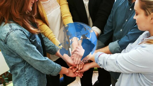 Animation of spinning globe over diverse colleagues stacking their hands together at office