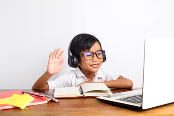 Happy asian elementary schoolboy raising hand while studying online using laptop at home