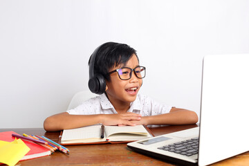 Happy asian elementary schoolboy studying online using laptop at home. Isolated on white background