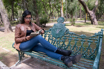 portrait of a beautiful latina woman sitting on a bench in the park reading a book