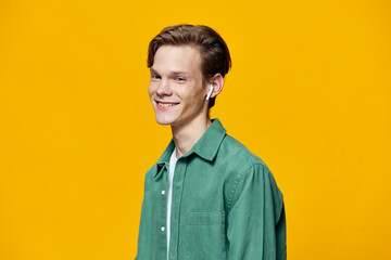 a guy in white wireless headphones stands against a yellow background in a green t-shirt. Horizontal photo with space for text