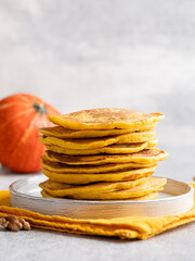 Pumpkin (squash) pancakes stack. Autumn breakfast, seasonal baing. Close up view. Orange crepes with honey and walnuts.