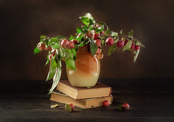 Branches of an apple tree with fruits in a vase and old books on a wooden table. Photo