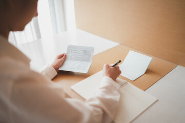 Right hand of asian woman are recording expenses in a notebook and left hand holding account book,plan and financial concept.