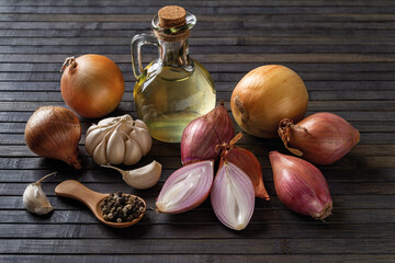 Whole and halved red shallot, yellow onion, garlic, peppercorns and olive oil on a black wooden background. Raw onion bulb for spice and seasonings concept. Organic vegetables. - obrazy, fototapety, plakaty