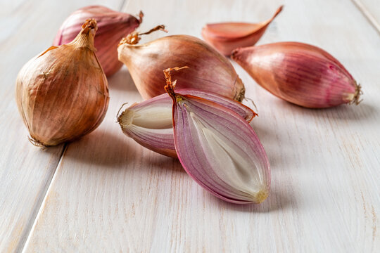 Halved red eschalot and whole bulbs on a white wooden table. Unpeeled long and round shallots close-up. Raw spring onion ready for cooking. Shallot organic vegetable concept.