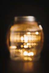 Large glass mason jar filled with pretty fairy lights set against a black background. Shot in bokeh out of focus style for abstract design image. Copy space available