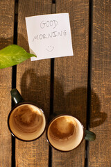 Nota de buenos días "good morning", dos cafés vacíos y sobre la madera sombra de corazón. Mañana de pareja de enamorados