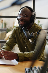 Young cheerful black man in headphones speculating on topical subject or curious news while sitting...