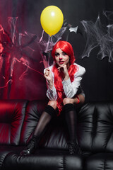 sexy woman in clown makeup and black knee socks holding yellow balloon near spiderweb on dark background.