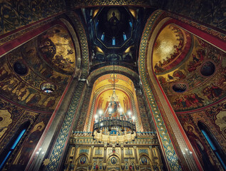Fototapeta na wymiar Interior architectural details of the Curtea de Arges monastery. The tall hall with painted icons, the golden altar and a chandelier with lights suspending out of ceiling