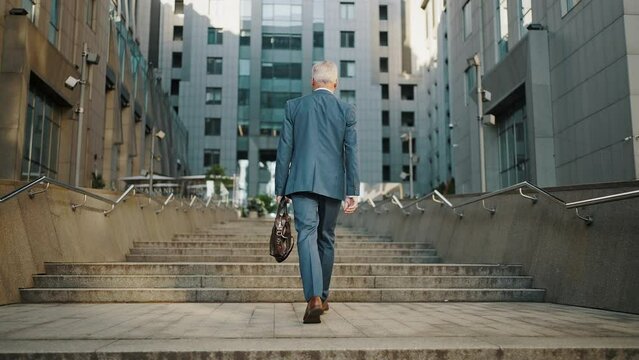 Senior businessman walks on stone stairs to office building