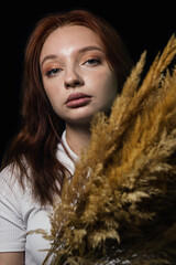 Portrait of a girl with cane branches on a black background. Young girl with red hair