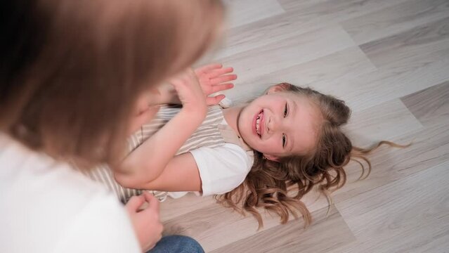 mom-daughter relationship, happy female child having fun playing with mom tickling lying on floor, close-up