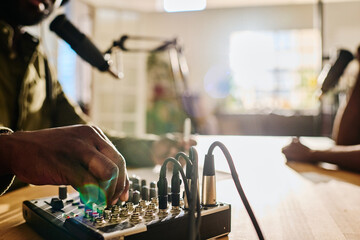 Hand of young African American man rotating consoles on soundboard while regulating sound before recording new audio file