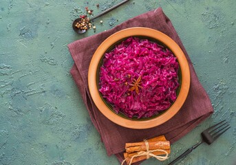 Fototapeta na wymiar Stewed red cabbage with spices in a clay dish on a green concrete background. Traditional Christmas food.