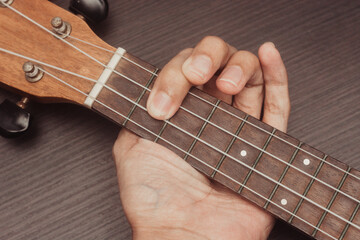 ukulele in close up with hand placing chords. The chord is F. Portable string instrument. Music creation concept. Isolated wooden background.